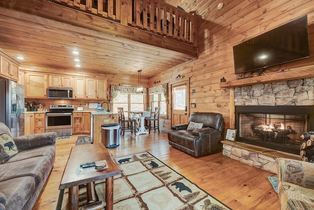 living area with light wood-style flooring, a stone fireplace, wood ceiling, a towering ceiling, and wood walls