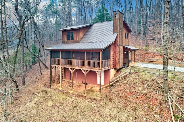 rear view of house with a view of trees, a chimney, and a sunroom