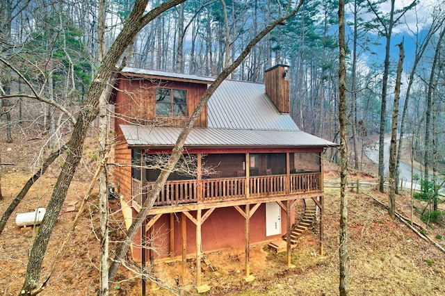 exterior space with stairs, a chimney, a sunroom, and metal roof