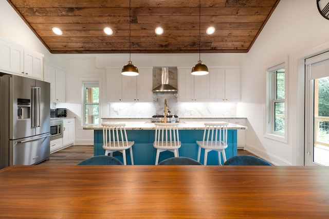 kitchen with a breakfast bar, decorative light fixtures, a center island with sink, stainless steel appliances, and wall chimney range hood