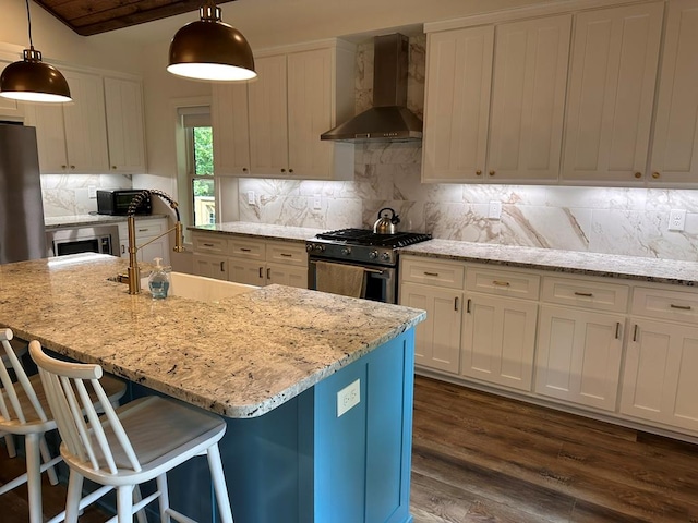 kitchen featuring a breakfast bar area, high end range, hanging light fixtures, a kitchen island with sink, and wall chimney range hood