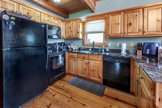 kitchen with beamed ceiling, sink, dark stone countertops, black appliances, and light wood-type flooring