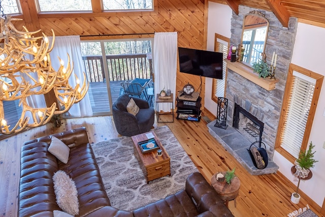 living room with hardwood / wood-style floors, wooden walls, a high ceiling, a notable chandelier, and a stone fireplace