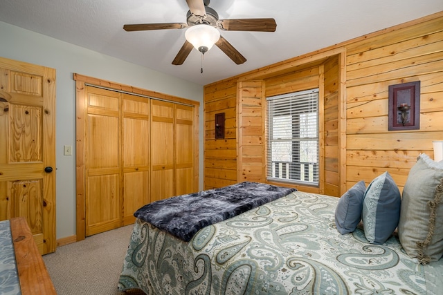 bedroom with a closet, wooden walls, light colored carpet, and a ceiling fan