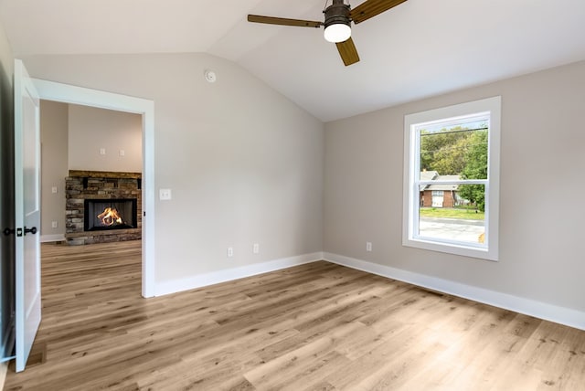 spare room with light hardwood / wood-style floors, vaulted ceiling, a fireplace, and ceiling fan