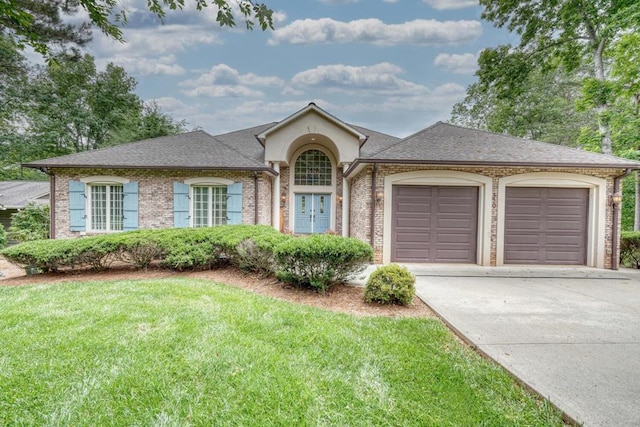 single story home with a front lawn, driveway, roof with shingles, an attached garage, and brick siding