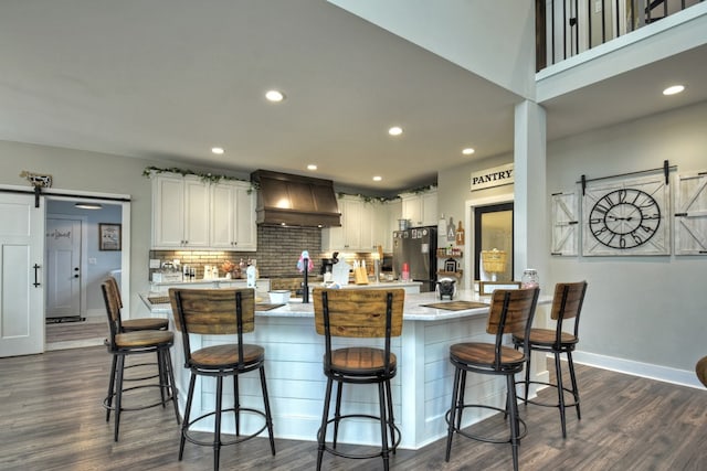 kitchen with white cabinetry, a barn door, a kitchen island with sink, and a kitchen breakfast bar