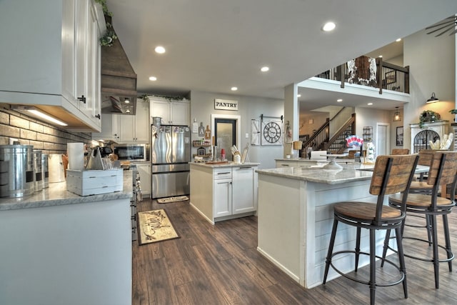 kitchen featuring appliances with stainless steel finishes, dark hardwood / wood-style floors, light stone countertops, white cabinets, and a kitchen island