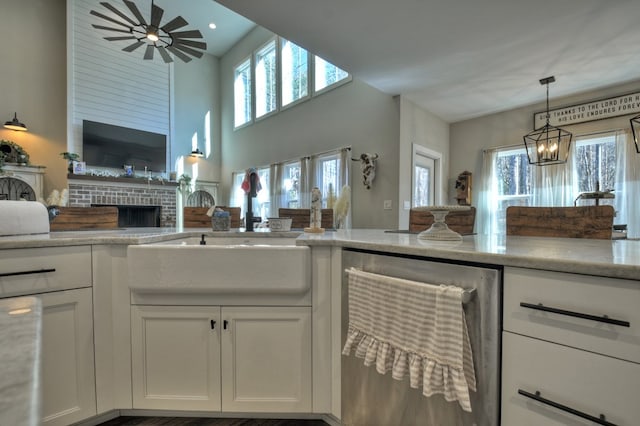 kitchen featuring sink, hanging light fixtures, white cabinets, a brick fireplace, and stainless steel dishwasher