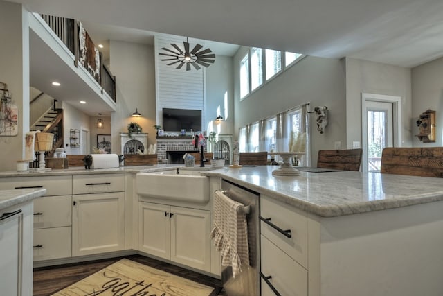 kitchen with sink, ceiling fan, light stone countertops, white cabinets, and a brick fireplace