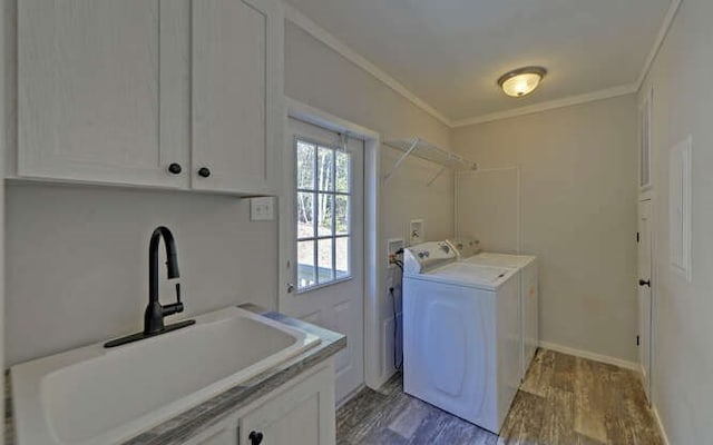 clothes washing area with ornamental molding, washing machine and dryer, a sink, wood finished floors, and baseboards