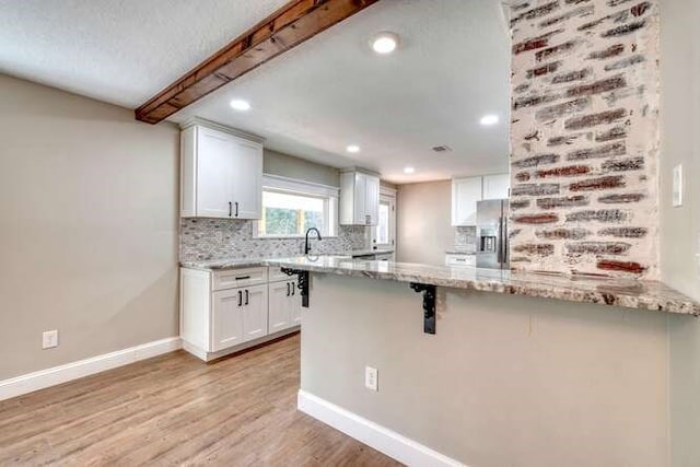 kitchen featuring kitchen peninsula, light stone counters, light hardwood / wood-style floors, white cabinetry, and a breakfast bar area