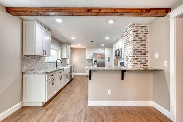 kitchen with backsplash, white cabinets, light hardwood / wood-style flooring, appliances with stainless steel finishes, and kitchen peninsula