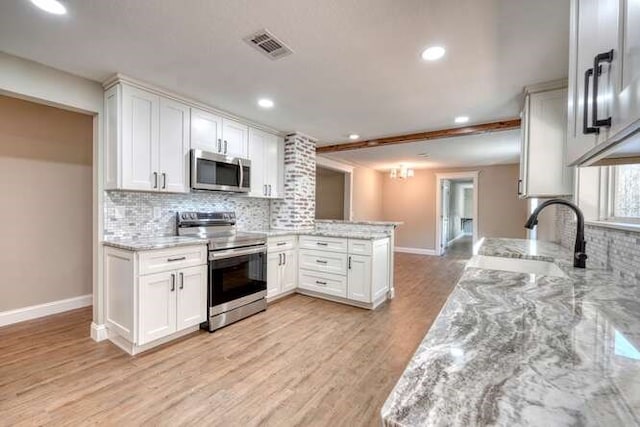 kitchen with kitchen peninsula, stainless steel appliances, white cabinetry, and light stone counters