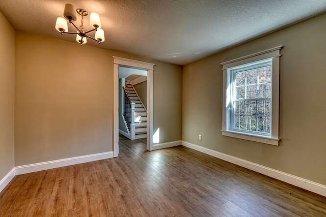 unfurnished room with a chandelier, wood-type flooring, and a textured ceiling