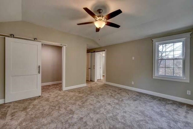 unfurnished bedroom featuring light carpet, a barn door, ceiling fan, and lofted ceiling