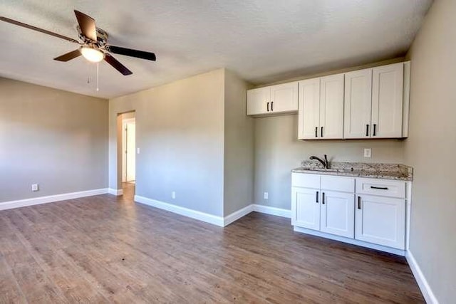 kitchen with light stone countertops, dark hardwood / wood-style floors, white cabinetry, and sink