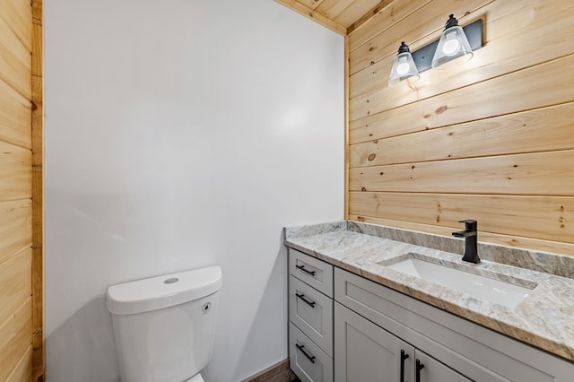 bathroom featuring wood walls, toilet, and vanity