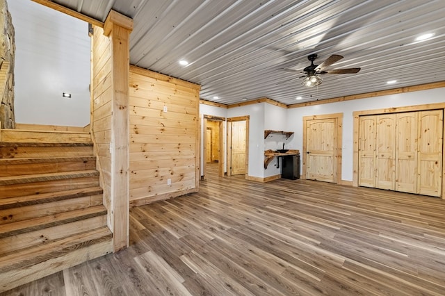 unfurnished living room with hardwood / wood-style flooring, ceiling fan, and wooden walls