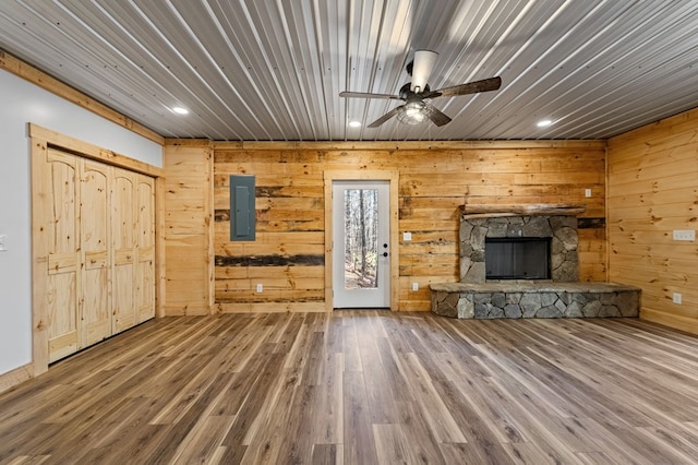 unfurnished living room with a stone fireplace, wood walls, electric panel, and wood-type flooring