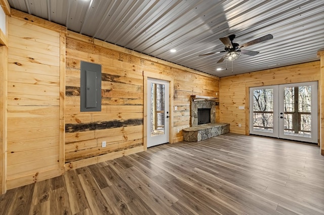 unfurnished living room with a fireplace, wood walls, electric panel, and french doors