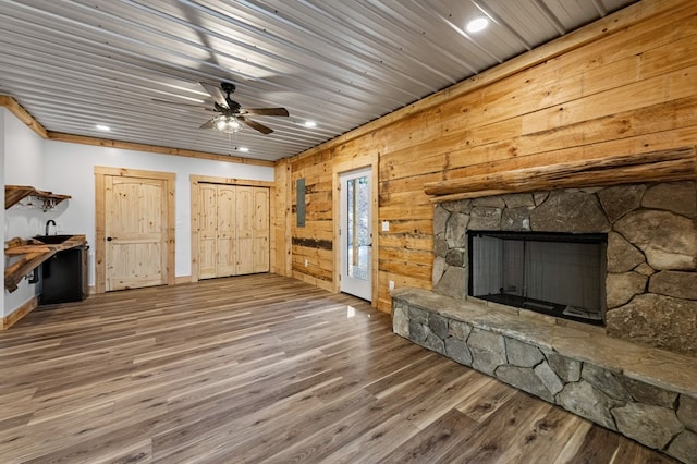 unfurnished living room with ceiling fan, hardwood / wood-style floors, wooden walls, and a fireplace