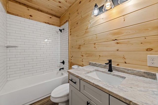 full bathroom featuring toilet, vanity, tiled shower / bath, and wooden walls