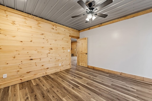 spare room featuring ceiling fan, wood walls, and wood-type flooring