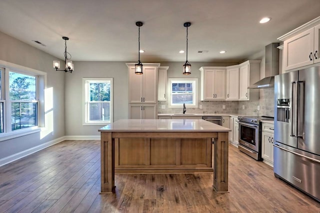 kitchen featuring wall chimney range hood, light countertops, a healthy amount of sunlight, and appliances with stainless steel finishes