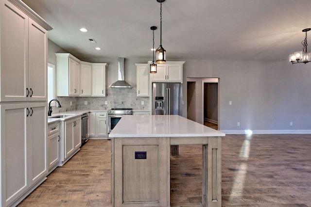 kitchen with wall chimney exhaust hood, stainless steel appliances, wood finished floors, and a sink