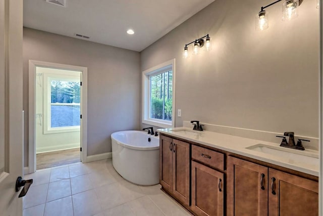 full bath featuring tile patterned flooring, a freestanding tub, visible vents, and a sink
