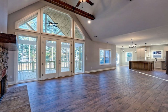 unfurnished living room with baseboards, ceiling fan with notable chandelier, dark wood-type flooring, a fireplace, and beam ceiling