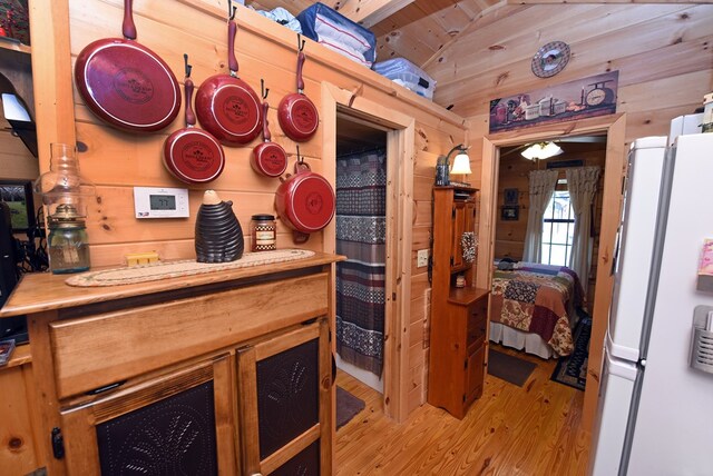 kitchen with light wood-type flooring, vaulted ceiling, white refrigerator, and wood walls