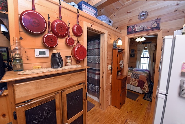 bedroom with light wood-type flooring, lofted ceiling, wood walls, and white refrigerator