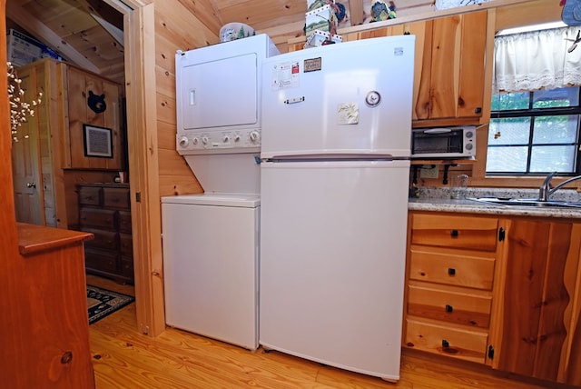 laundry area with wood walls, stacked washer / dryer, sink, and light hardwood / wood-style floors