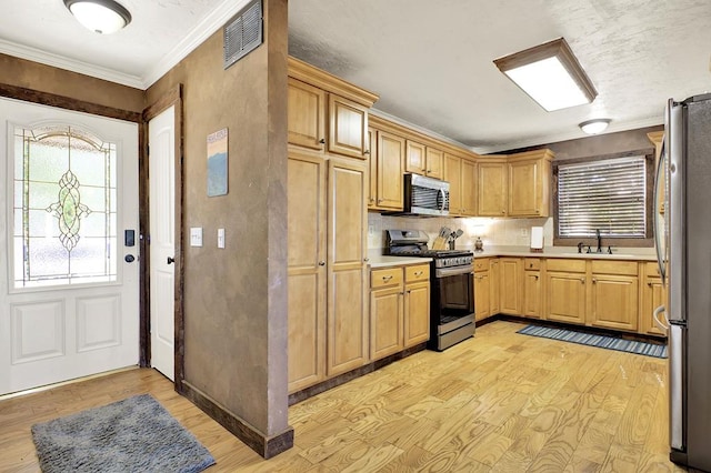 kitchen with backsplash, sink, crown molding, appliances with stainless steel finishes, and light hardwood / wood-style floors