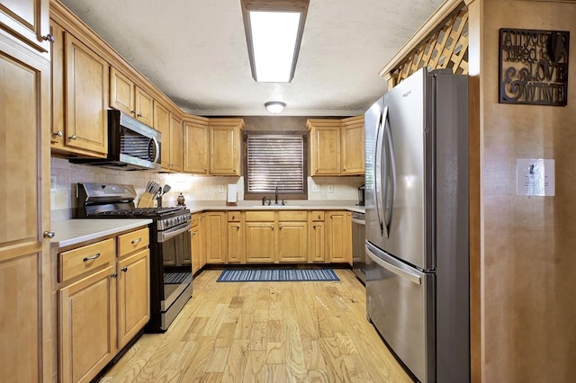 kitchen with sink, light hardwood / wood-style flooring, decorative backsplash, and stainless steel appliances