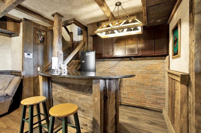 bar with brick wall, dark brown cabinets, and wood-type flooring