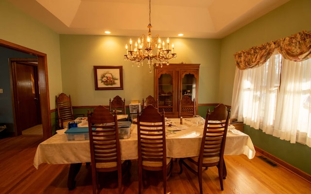 dining area featuring a raised ceiling, wood-type flooring, and an inviting chandelier