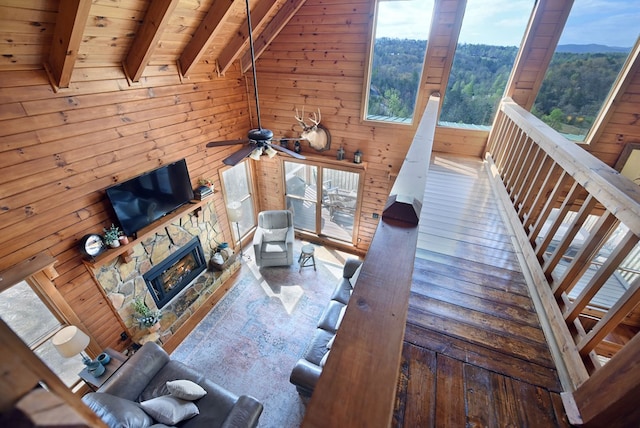 living room with a fireplace, wood ceiling, ceiling fan, wooden walls, and beam ceiling