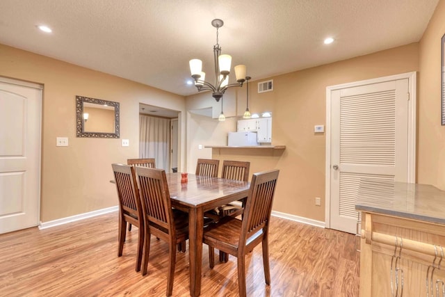 dining room with an inviting chandelier, light wood-type flooring, and a textured ceiling