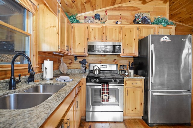 kitchen with wood walls, sink, light stone countertops, and stainless steel appliances