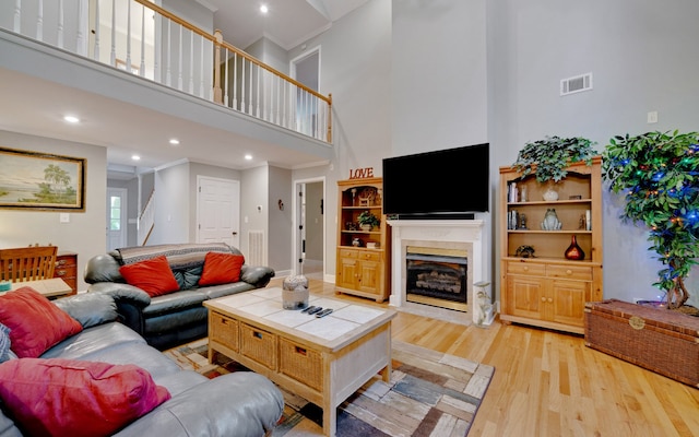 living room featuring light wood-type flooring, crown molding, a high ceiling, and a fireplace