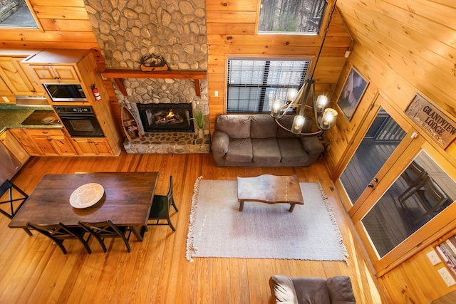 living room featuring hardwood / wood-style flooring, a stone fireplace, a towering ceiling, and wooden walls