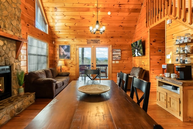 dining space featuring wooden walls, light hardwood / wood-style floors, high vaulted ceiling, and french doors