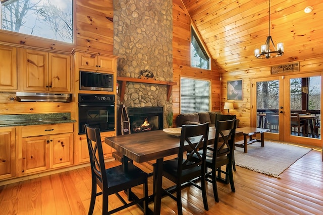 dining space featuring french doors, light hardwood / wood-style flooring, high vaulted ceiling, a notable chandelier, and a stone fireplace