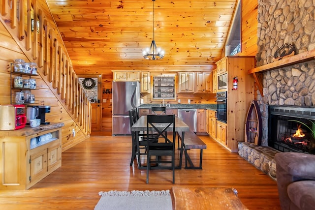 dining area featuring light wood-type flooring, wooden walls, high vaulted ceiling, a notable chandelier, and a stone fireplace