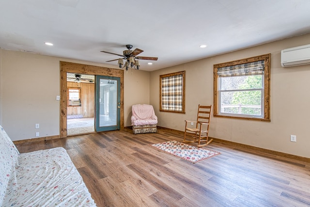 sitting room with a ceiling fan, an AC wall unit, recessed lighting, and wood finished floors