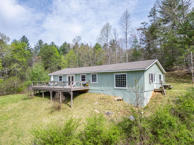 back of house featuring a lawn, roof with shingles, a deck, and a wooded view