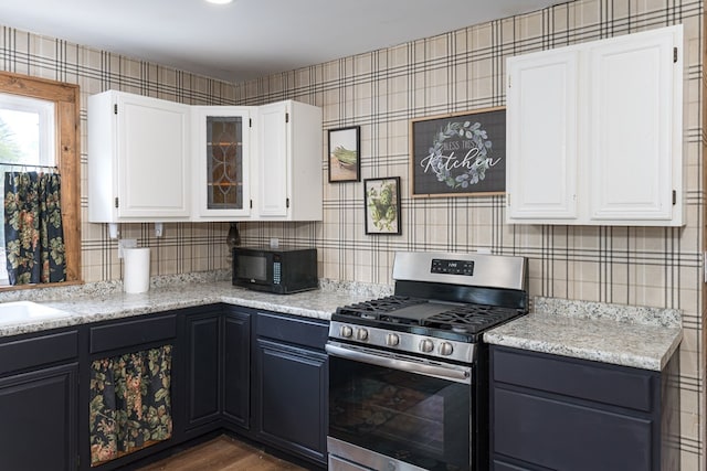 kitchen with black microwave, gas stove, white cabinetry, dark wood-type flooring, and glass insert cabinets